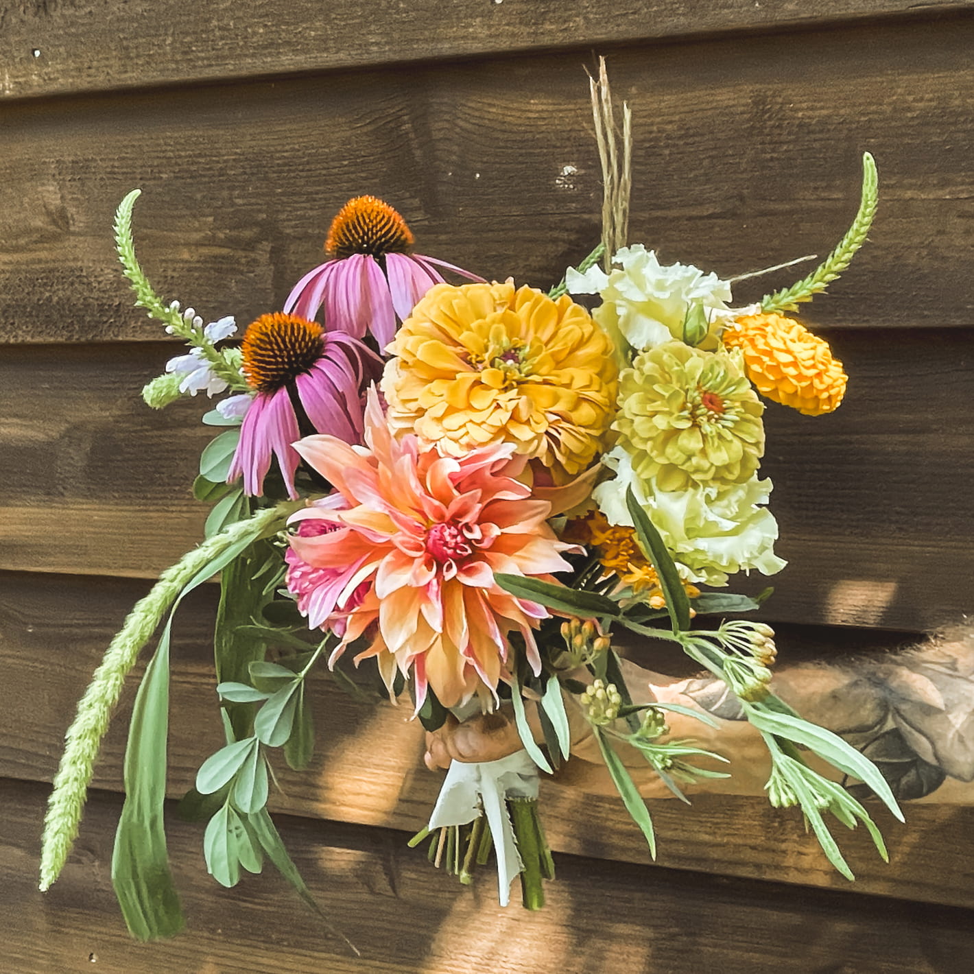 A lush mixed-dahlia bouquet in autumn tones against a wooden wall.